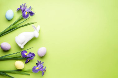 Easter eggs and irises flowers on light green background with space for text, top view.