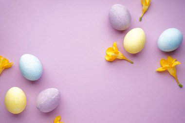 Easter eggs and freesia flowers on a purple background, space for text, flat lay.