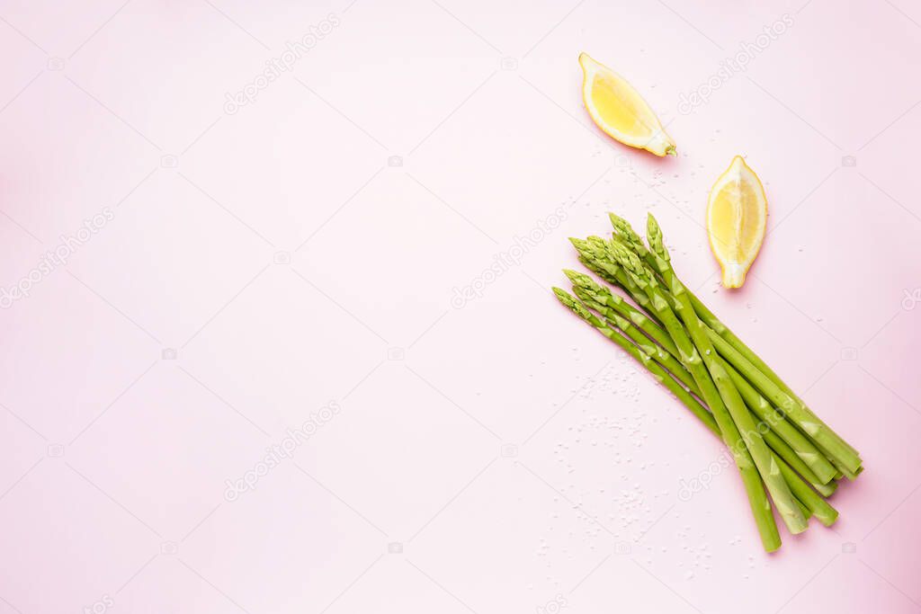 Fresh green asparagus and lemon wedges on pink background, space for text. Top view