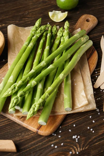 Fresh asparagus on kitchen wood board on wooden background, close-up.