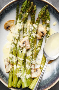 Gri arka planda bir tabakta soslu kuşkonmaz ve mantar, yakın plan. Üst görünüm.