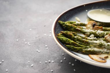 Gri arka planda bir tabakta soslu kuşkonmaz ve mantar, yazı için yer, yakın plan..