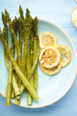 Ahşap arka planda bir tabakta limonlu fırında kuşkonmaz. Düz yatıyordu.