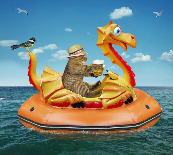 A beige cat in a straw hat with a mug of beer is floating on an inflatable dragon in the sea at a resort.