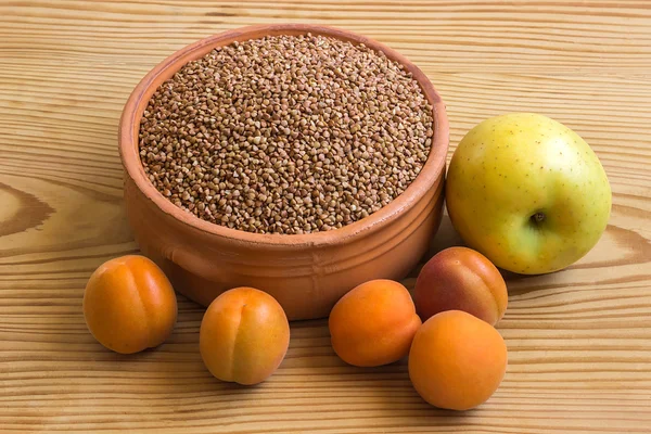 Buckwheat in a ceramic bowl next to the apple and apricots on wo — Stock Photo, Image
