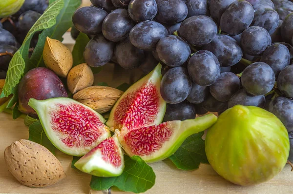 Bodegón de frutas frescas de colores. Ramo de uvas negras, higos verdes sobre un fondo claro. Pan en el paquete de papel . —  Fotos de Stock