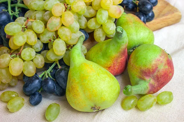 La naturaleza muerta - la fruta brillante sobre la tela clara. Uvas negras y verdes vintage, pera fragante . —  Fotos de Stock