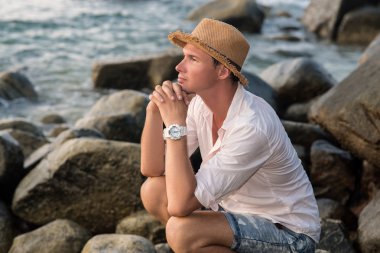 plajda kayalar üzerine oturan adam