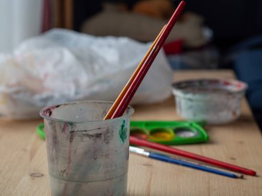 Boya fırçaları ve sanat malzemeleri ahşap bir masaya dizilmiş, rahat bir sanatsal çalışma alanı yaratıyor. Resim araçları, doğal ışık ve kopyalama alanı ile yaratıcı natürmort yaşam, sanat, yaratıcılık ve DIY kavramları için idealdir.