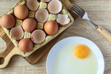 Mutfakta çiğ yumurta ve yumuşak doğal ışık olan bir tabağın yanındaki ahşap bir tahtanın üzerinde kırılmış yumurtalar. Yemek, ev yemeği ve yemek tarifi..
