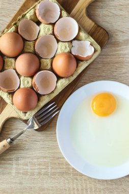 Mutfakta çiğ yumurta ve ahşap bir tabağın yanında kırık yumurtaların olduğu bir fotoğraf. Yemek ve ev yapımı tarif kavramı.