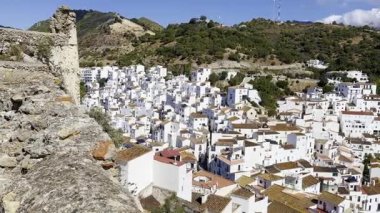 Casares Kalesi 'nden gelen yatay tava, yoğun gün ışığı altında duvarlarını ve beyaz köyü gösteriyor. Güçlü bir zıtlık ve açık gökyüzü ile tipik Endülüs manzarası.