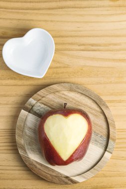 Elmaya kazınmış kalbin yakın çekimi ve küçük beyaz kalp şeklinde bir tabak.