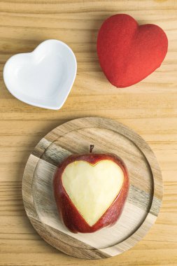 Elmaya kazınmış kalbin yakın çekimi, küçük beyaz kalp şeklinde bir tabak, ve kırmızı bir kalp.