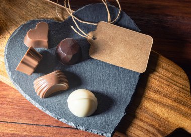 Siyah bir tahta kalbe koyu ve sütlü çikolatalı bonbonlar yerleştirilmiş. Minimalist bir Sevgililer Günü kompozisyonu..