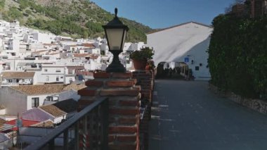 Bir terastan tarihi Mijas merkezinin sağdan sola panoramik görüntüsü, tipik beyaz evleri, kırmızı çatıları, çiçek saksıları ve parmaklıkları olan sokakları ve yürüyen insanları gösteriyor. Mijas, Malaga, Endülüs, İspanya, 21 Şubat 2026.