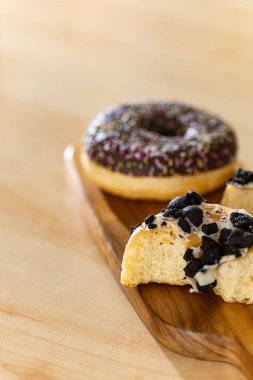 Isırılmış beyaz ya da siyah çikolatalı çöreği parlak bir mutfakta, tahta bir tahtanın üzerinde, yumuşak doğal yan ışık ve bulanık arka plan. Hoşgörü kavramı, arzu ve tatlı yemek anı..