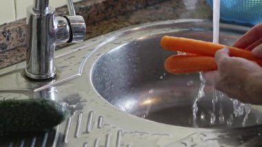 Ön planda bulanık sebzeli yatay video. Eller lavabo musluğunun altında bir havuç yıkıyor, sonra suyu kapatıp ellerini kurutuyor. Salata hazırlığı ve sağlıklı yemek..