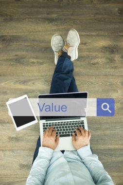 Genç adam dizüstü bilgisayarla yerde oturuyor.