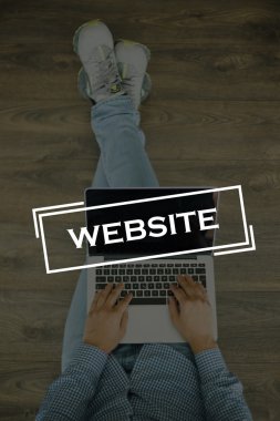 Genç adam dizüstü bilgisayarla yerde oturuyor.