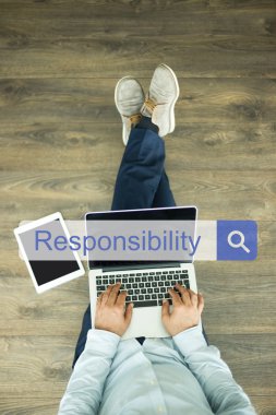 Genç adam dizüstü bilgisayarla yerde oturuyor.