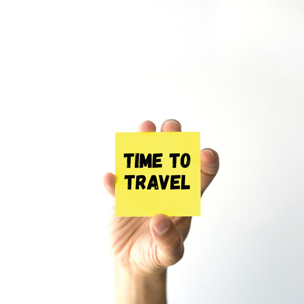 Hand holding yellow sticky note written TIME TO TRAVEL word