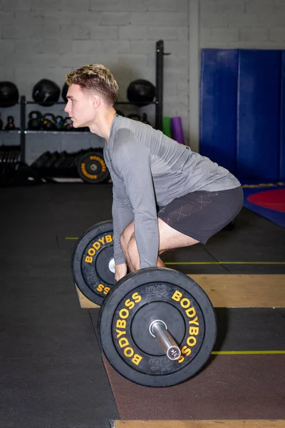 Genç sporcular spor salonunda halterle antrenman yapıyor.