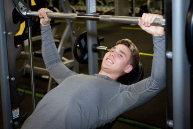 Genç sporcular spor salonunda halterle antrenman yapıyor.