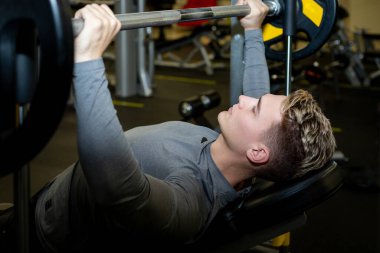 Genç sporcular spor salonunda halterle antrenman yapıyor.