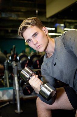 Genç sporcular spor salonunda dambıllarla antrenman yapıyor.