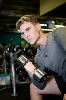 Genç sporcular spor salonunda dambıllarla antrenman yapıyor.