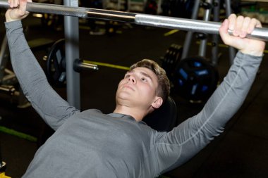 Genç sporcular spor salonunda halterle antrenman yapıyor.