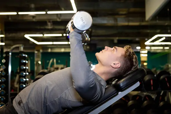 Genç sporcular spor salonunda dambıllarla antrenman yapıyor.