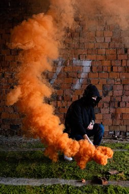 Siyah kapüşonlu, turuncu yakıtlı genç, yakışıklı suçlu bir adam. Turuncu duman şenlik ateşi. Sıcak ve patlama, yanan gaz, tehlike ve cehennem. Siyah maske, kişinin protestosu