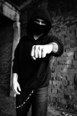 Siyah maskeli yakışıklı suçlu gangster adam, Coperid Coronavirus 'a karşı. Kapüşonlu protesto ya da turuncu tuğlalı duvarın yanındaki kapüşonlu protesto. Güç, saldırganlık ve savaşa hazır olmak. şehir hayatı