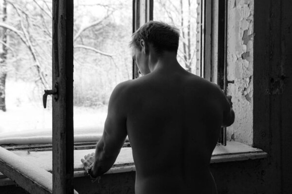 Голые молодые красивые модели мужчины с мускулистым телом и туловищем, стоящие у окна в заброшенном здании. Черно-белая фотография.