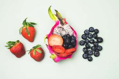 Açık Yeşil Arkaplan Üst Görünümü 'nde Yarım Ejderha Meyvesi ve Çiğ Çilek ve Yabanmersini Servisli Egzotik Meyve Salatası