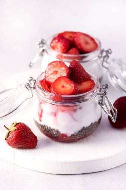 Sağlıklı Çilek Kahvaltısı Hindistan cevizi sütü ve Chia tohumları kavanozlarda Gri Arka plan Dikey