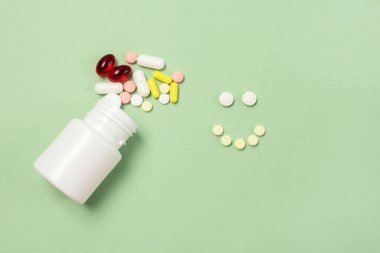 Beyaz haplar şişesi ve yeşil arka plandaki haplardan yapılmış mutlu bir yüz.