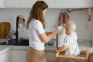 Anne ve bebek mutfak aktivitesi yapıyor, erken yaşam becerileri ve sağlıklı yemek alışkanlıkları öğretiyor, evde yemek pişirirken aile bağı kuruyor.