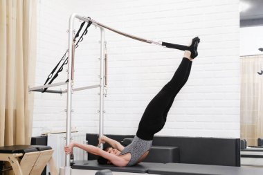 Kadın pilates reformatörü eğitimi ters çevirme tekniğiyle, çekirdek dayanıklılık ve omurga basınç azaltma terapisi için ileri esneklik egzersizi yapıyor. Derin çekirdek aktivasyonu ve omurga hizalaması