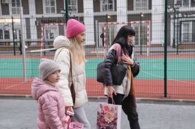 Arkadaşlar, modern yerleşim alanındaki oyun parkında, kış mevsiminde, çağdaş kentsel yerleşim ortamında küçük bir çocukla dışarıda eğleniyorlar.