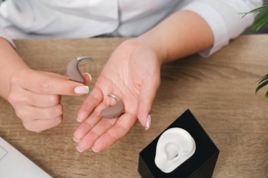 Modern dijital işitme cihazları odiyologların elinde klinikte. Doktor işitme cihazını tutuyor. Uyum ve gösteri için kulak modelinin yanında. Yakın çekim, üst görünüm