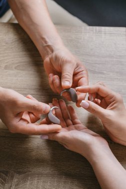 Odiyoloji uzmanının klinikteki hastaya modern işitme cihazı vermesi. Açık kasa ve kulaklık aksesuarlarıyla işitme aygıtı gösterimi.