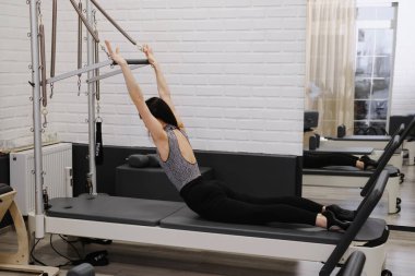 Çağdaş stüdyoda ileri düzey çekirdek ve bacak güçlendirme egzersizleri yapan, direnç kablolarıyla pilates kulesi teçhizatı eğitimi alan kadın.