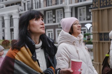 40 'lı yaşlardaki kadın arkadaşlar modern yerleşim alanlarında birlikte yürüyorlar, kış kıyafetleri giyiyorlar, modern şehir ortamında boş zamanların tadını çıkarıyorlar.