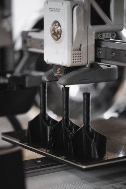 Endüstriyel 3D yazıcı ekstraktörü, katkı maddesi üretimi sırasında plakaya çoklu siyah plastik parçalar basıyor. Isıtılmış 3D yazıcı nozülünün yakın plan görüntüsü