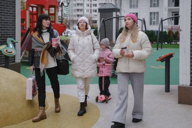 Arkadaşlar, modern yerleşim alanındaki oyun parkında, kış mevsiminde, çağdaş kentsel yerleşim ortamında küçük bir çocukla dışarıda eğleniyorlar.