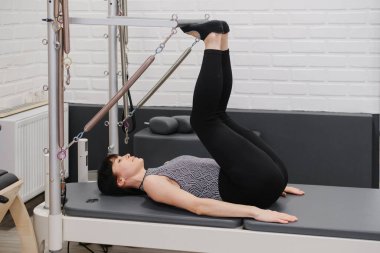 Çağdaş stüdyoda ileri düzey çekirdek ve bacak güçlendirme egzersizleri yapan, direnç kablolarıyla pilates kulesi teçhizatı eğitimi alan kadın.