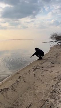 Issız bir sahilde dramatik bulutlu bir gökyüzü altında yürüyen bir adamın arka görüntüsü. Huzurlu doğa manzarası. Bahar ya da kışın nehir kenarında. Dikkatli yürüyüş ve huzurlu anlar